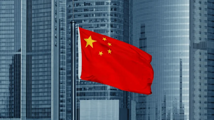 Flag of China waving on a pole, with skyscrapers in the background