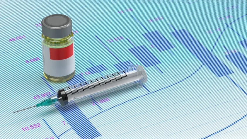 Syringe next to a pharmaceutical drug, on top of financial charts