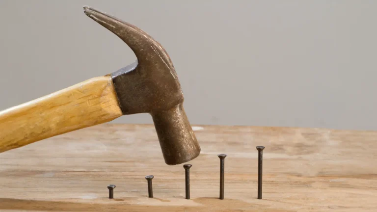 Hammer hitting nails on a wooden plank, each nail increased in height