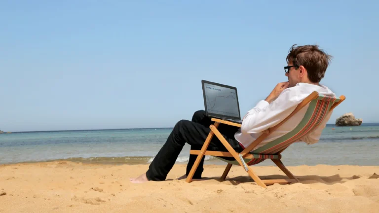 A man sitting in a chair on the beach with a laptop in his lap